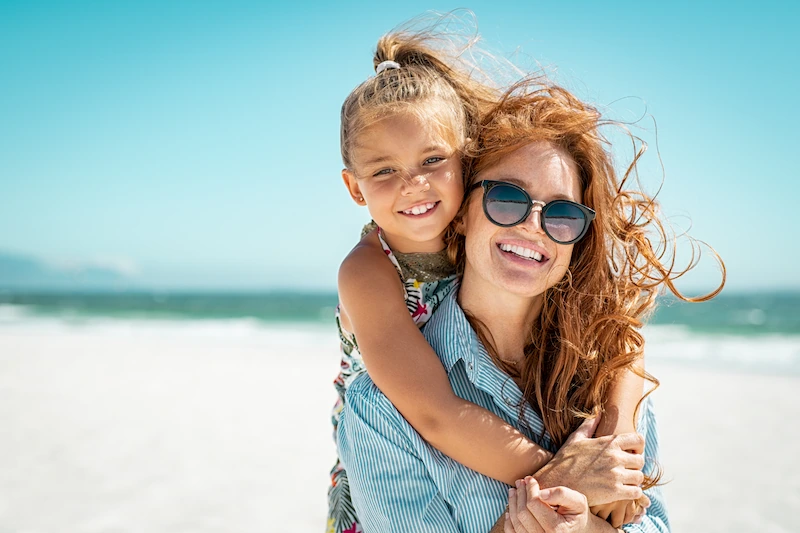 mother and daughter smiling on beach sunny day